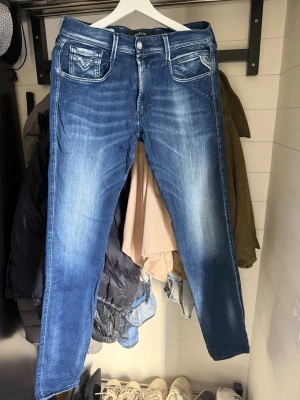 Blå jeans från Replay med tvättad look - Säljer ett par blå jeans från Replay med snygg tvättad effekt och kontrastsömmar. Klassisk femficksmodell med raka ben och detaljerade bakfickor. Jeansen har en modern passform och är tillverkade i mjukt denimtyg.