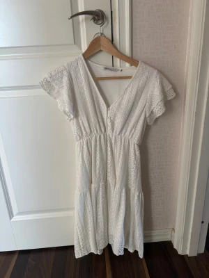 Vit spetsklänning med volangärm - Söt vit klänning i spets med v-ringning och volangärmar. Klänningen har en omlottkänsla upptill, markerad midja och faller i flera lager. Använd endast gång! Perfekt till skolavslutningen. Klänningen är i storlek xs men passar mig som brukar ha S.