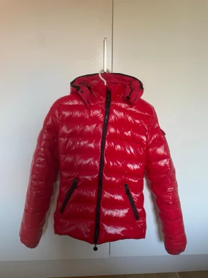 Dunjacka från Moncler - Snygg röd dunjacka från Moncler med glansig finish, huva och svarta dragkedjor. Är i storlek 2 som motsvarar M men passar även mig som har S. Är inte använd mycket så i väldigt fint skick! 