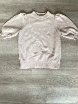 Ljusrosa stickad topp Vero Moda - Supersöt ljusrosa stickad topp från Vero Moda med puffärmar och ribbade muddar. Tröjan har en högre rund halsringning och är gjord i mjukt material som känns skönt mot huden. Perfekt för dig som gillar en feminin och trendig stil.