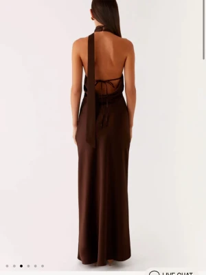 Brun långklänning med öppen rygg - Snygg brun långklänning med halterneck och öppen rygg. Klänningen har snörning baktill och ett elegant fall i material som ser ut som satin eller polyester. Perfekt för dig som vill ha en stilren och trendig look. Perfekt nu inför balen ! Alla lappar kvar och den är helt ny, då jag hittade en annan inför balen 💞ca 2 000 nypris ihop med frakten till Sverige ! 