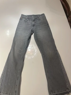 Grå flare Zara jeans med råa kanter - Säljer ett par grå jeans med rak passform och råa, fransiga benslut. Jeansen har klassisk femficksdesign och är tillverkade i denim. Perfekta för en avslappnad och trendig look. Storleken motsvarar ungefär 30/32 i vanliga jeans. 183 cm lång 64 kg på personen i bilderna.