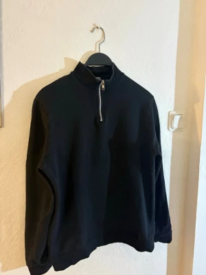Svart halfzip tröja asos design - En svart långärmad tröja från asos design med halv dragkedja framtill och hög krage. Tröjan har en enkel och clean design, perfekt för lager på lager och funkar till det mesta. Tillverkad i mjukt material för skön känsla.