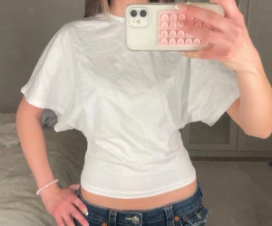 Nelly topp - Vit t-shirt med loose passform och korta ärmar. Enkel och stilren design med rund halsringning. Perfekt till jeans eller shorts för en avslappnad look. Tillverkad i mjukt bomullstyg.