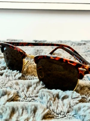 Ray-Ban Clubmaster solglasögon brun - Säljer ett par Ray-Ban Clubmaster solglasögon med brunsköldpaddsmönstrad båge och gulddetaljer. Klassisk retroform med mörka glas. Kommer med originalfodral, putsduk och box. Perfekta för dig som vill ha en tidlös och snygg accessoar.