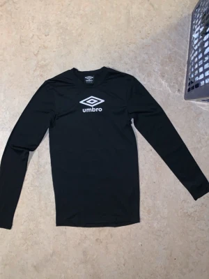 S. Svart långärmad tight träning Umbro  - Helt ny aldrig använd Köpte den till min lillebror för han börjat gymma köpte fel storlek han hade M råka Köpa S istället med misstag uttan prislapp köpte som en present Svart långärmad träningströja från Umbro med vitt logotryck på bröstet. Tillverkad i ett stretchigt och lätt material som passar perfekt för sport och träning som ger en muskulös look tight på kroppen bra för alla sporter Enkel och stilren design med rund hals.