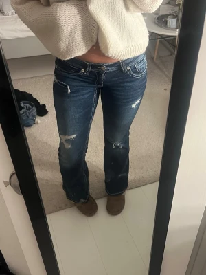 Mörkblå bootcut jeans med slitningar - Snygga mörkblå bootcut jeans med slitningar och ljusa detaljer. Jeansen har dekorativa sömmar på bakfickorna och klassisk femficksdesign. Perfekta för dig som gillar en avslappnad och trendig stil.
