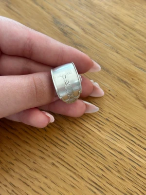 Silverring - Unik silverring med bred design och elegant gravyr av blommönster. Ringen har en matt finish och är tillverkad i silver, vilket ger den en stilren och tidlös look. Perfekt för dig som gillar detaljer och vill sticka ut.