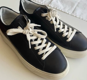 Svarta sneakers med vit sula - Snygga svarta sneakers med vit tjock sula och vita skosnören. Skorna har en klassisk låg modell och är tillverkade i slätt läder med vit insida. Perfekt för dig som vill ha en stilren och enkel look. Från Ecco.                    
