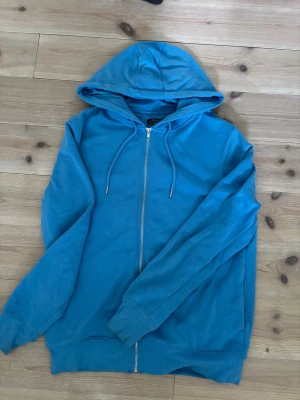 Blå zip-hoodie från  - Snygg blå hoodie från Primark i storlek medium. Modellen har dragkedja framtill, huva med dragsko och ribbade muddar vid ärmslut och nederkant. Perfekt för en avslappnad och chill stil.