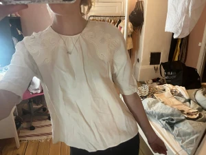 Vit blus med spetsdetaljer - Säljer en vit blus med fina spetsdetaljer på axlarna och korta ärmar. Blusen har en rak passform och dragkedja i ryggen. Perfekt för en stilren och fräsch look.