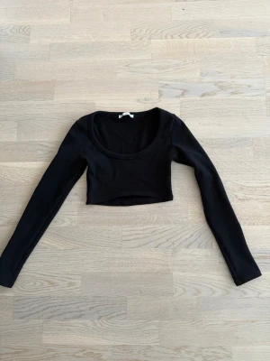 Svart croppad långärmad topp, strl S - Snygg svart croppad topp med långa ärmar och rundad urringning. Perfekt att styla med höga jeans eller kjol för en trendig look. Tillverkad i mjukt bomullsmaterial som sitter skönt mot kroppen.
