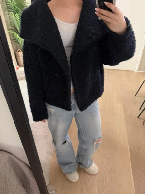 Svart teddyjacka med stor krage - Mysig svart teddyjacka från Zara med oversized passform och stor, bred krage. Jackan har knäppning framtill och är tillverkad i ett fluffigt teddy-material som ger en cool och avslappnad look. Perfekt för att hålla värmen under kyliga dagar.