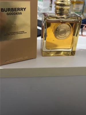Burberry Goddess Eau de Parfum 100ml - Burberry Goddess Eau de Parfum Intense i en lyxig, fyrkantig glasflaska med guldfärgad detalj och lock. Parfymen har en elegant, gyllene vätska och kommer i en stilren beige kartong med gulddetaljer. Perfekt för dig som gillar exklusiva dofter.köpte den för 2150 men säljer den för 1250