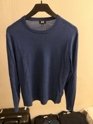 Merino ull tröja från Uniqlo - Snygg blå stickad tröja från Uniqlo med rund halsringning och långa ärmar. Tröjan är tunnstickad och har en klassisk, stilren design som passar perfekt till jeans eller chinos. Materialet känns mjukt och följsamt mot kroppen.