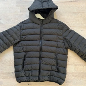 Svart pufferjacka från Colmar - Säljer en svart pufferjacka från Colmar med huva och dragkedja framtill. Jackan har två fickor med dragkedja och ett diskret Colmar-märke på ärmen. Perfekt för kyliga dagar och enkel att matcha med olika outfits. Storlek 54 men jackan är liten i storlek så passar L