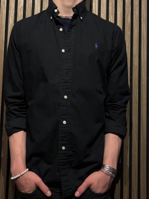 Svart skjorta från Ralph Lauren - Klassisk svart skjorta från Ralph Lauren med lila broderad logga på bröstet. Storlek S!