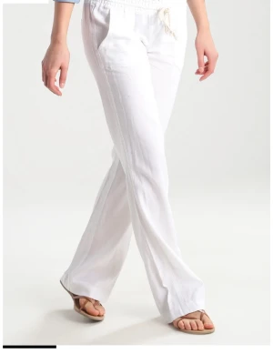 Vita roxy linnebyxor  - Säljer ett par vita linnebyxor med avslappnad passform och dragsko i midjan. Byxorna har raka ben och sidofickor, perfekta för en chill och stilren look. Dom är lite för korta för mig som är 164cm lång och dom är uppsydda sen innan