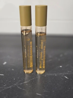 Rituals parfym i guldiga flaskor - Två eleganta parfymflaskor från Rituals med guldiga lock och transparent glas. Flaskorna har en stilren, cylindrisk form och innehåller en gyllene vätska. Perfekt för dig som gillar exklusiva och snygga dofter.
