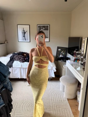 Gul långklänning med spets  - Säljer en snygg gul långklänning med spetsmönster och coola cut-outs vid midjan. Klänningen har halterneck och är axelbandslös, vilket ger en trendig look 🌟nypris 525kr + frakt 