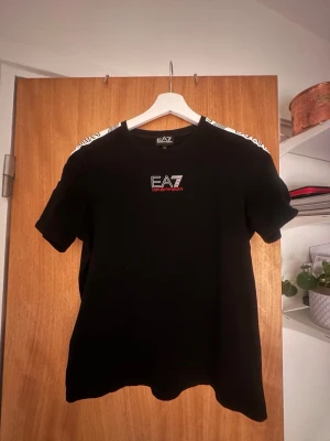 Svart EA7 Emporio Armani t-shirt - Snygg svart t-shirt från EA7 Emporio Armani med logga på bröstet och vita detaljer på axlarna. Klassisk passform och rund halsringning. Perfekt för dig som gillar stilrena märkeskläder.