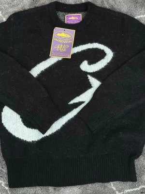 Corteiz stickad tröja  - Cool svart stickad tröja med stor vit grafisk detalj på framsidan. Tröjan har rund halsringning och ribbade muddar vid ärmslut och nederkant. Perfekt för dig som gillar streetwear och vill sticka ut lite extra.