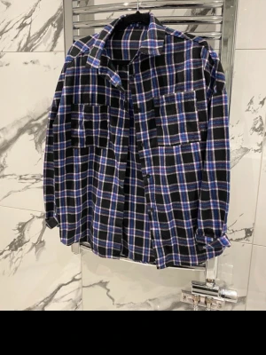 Rutig skjorta från Boohoo i blått och svart - Säljer en oversized rutig skjorta från Boohoo i svart, blått och vitt. Skjortan har två bröstfickor, klassisk krage och knappar framtill. Perfekt för en avslappnad och trendig look.