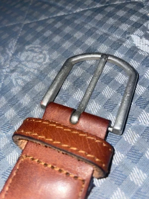 Brunt och marinblått flätat bälte - Snyggt bälte med brunt skinn i ändarna och marinblått flätat band. Spännet är i silverfärgad metall och bältet har klassisk design som passar till jeans eller chinos. Perfekt accessoar för att lyfta din outfit.