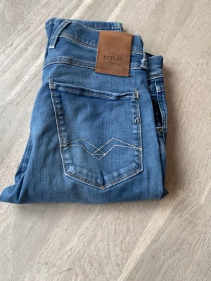 Replay anbass jeans  - Säljer ett par blå slim fit jeans från Replay Hyperflex med klassisk femficksmodell och snygga kontrastsömmar. Jeansen har en skön stretchig känsla och läderpatch bak i midjan. Perfekta för dig som gillar en modern och bekväm stil. Storlek 28/32