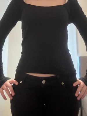 Svart långärmad topp  - En svart långärmad topp med snygg fyrkantig ringning och figurnära passform. Toppen är enkel och stilren, perfekt att matcha med jeans eller kjol. Materialet känns mjukt och stretchigt, vilket gör den bekväm att bära hela dagen.