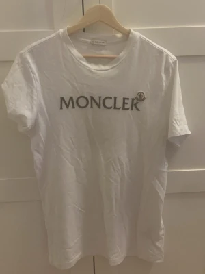 Äkta Vit Moncler t-shirt med logga - Snygg vit t-shirt från Moncler med klassisk logga tryckt på bröstet och en liten Moncler-patch. T-shirten har rund hals och korta ärmar, perfekt för en clean och stilren look. Köpt på NK i Stockholm