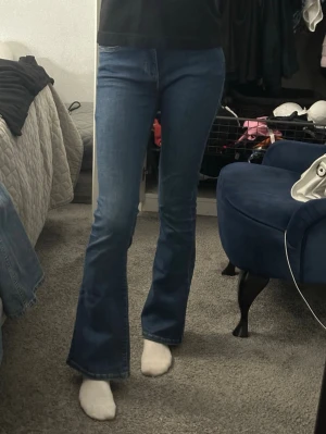 Stretchiga blå bootcut jeans med hög midja - Säljer ett par klassiska blå bootcut jeans med hög midja och utsvängda ben. Jeansen har fem fickor och stängs med dragkedja och knapp. Perfekta för dig som gillar en retroinspirerad look och vill ha ett par jeans som sitter snyggt över höfterna.