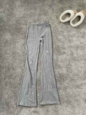 Grå mjukisbyxor med utsvängda ben - Säljer ett par grå mjukisbyxor med utsvängda ben och resår i midjan. Byxorna är gjorda i ett mjukt, tunt och stretchigt material som känns skönt mot huden. Byxorna har en liten färgfläck på ena låret men är lätt att ta bort.