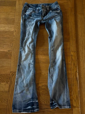 Blå bootcut jeans  - Snygga blå bootcut jeans från Amethyst med slitningar och ljusa tvättade partier. Midjemåttet är 34 cm och innerbenslängden är 75 cm