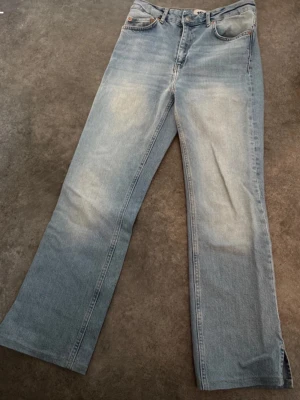 Ljusblåa bootcut jeans med slits - Säljer ett par ljusblå jeans i bootcut-modell med snygga slitsar nertill på benen. Jeansen har klassisk femficksdesign och är gjorda i denim med lätt tvättad look. Perfekta för dig som gillar en avslappnad och trendig stil. OBS byxan är uppsydd av sömerska och är nu, 66,5 cm från grenen och ner och själva slitsen är ca 7 cm