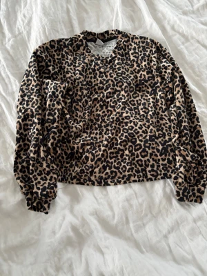 Leopardmönstrad långärmad tröja - Säljer en snygg långärmad tröja med leopardmönster i beige och svart. Tröjan har rund halsringning och är tillverkad i ett mjukt, stretchigt material som känns skönt mot huden. Perfekt för dig som vill sticka ut lite extra.🐆🐆🥰