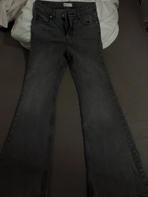 Gråa bootcut jeans från Gina Tricot - Säljer ett par gråa bootcut jeans från Gina Tricot. Jeansen har mid waist, klassisk femficksdesign och vida ben. Materialet är denim i bomull med en lätt tvättad look. Perfekta för en avslappnad och trendig stil.