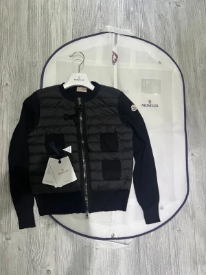 Moncler cardigan dam  - Hej! En Moncler cardigan för dam till salu. Jackan är i jättefint skick och har inga defekter eller liknande. Den är äkta och köpt online  kvittot finns. Jag säljer den pågrund av att den inte riktigt passar min stil. Den är jättefin och jag fick alltid jätte många komplimanger när jag andvände den. Moncler dustbag lapprna osv ingår med jackan. Hör av dig vid minsta lilla fråga! 💕