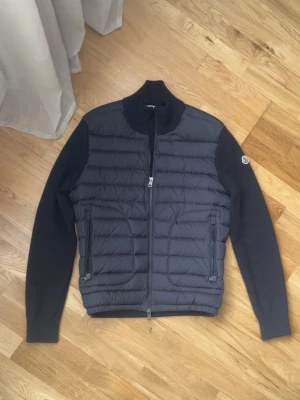 Svart cardiganjacka från Moncler - Snygg svart cardiganjacka från Moncler med quiltad front och stickade ärmar. Två dragkedjefickor och Moncler-logga på ärmen.  Perfekt för de som vill ha en stil ren stil. Kontakta över funderingar 