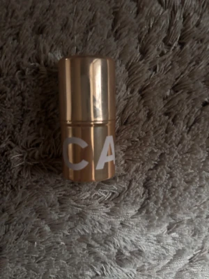 Guldig highlighter stick från CAIA - Highlighter i stickformat från CAIA med snygg guldig hylsa och krämig formula. Färgen är en skimrande champagne-ton som ger glow till kindben och andra highlights. Perfekt att ha i väskan för enkel applicering när som helst. Andvönt fåtal gånger