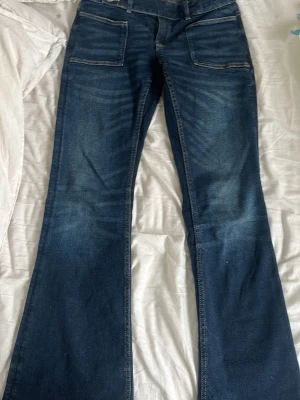 Blå utsvängda jeans Gina Tricot - Säljer ett par blå jeans från Gina Tricot med utsvängda ben och stora fickor framtill. Jeansen har en klassisk denimlook med kontrastsömmar och är tillverkade i ett slitstarkt bomullsmaterial. Perfekta för dig som gillar retrostil och vill ha ett par bekväma jeans. De är low waist. Använt bara 2-3 gånger