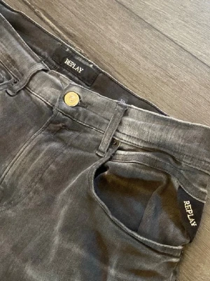 Gråa Replay jeans med raka ben - Säljer ett par gråa jeans från Replay med raka ben och klassisk femficksmodell. Jeansen har en snygg tvättad look och detaljer som guldfärgad knapp och Replay-logga vid fickan. Perfekta för en avslappnad och trendig stil.