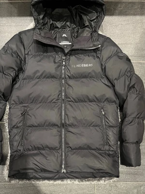 J.Lindeberg Vinterjacka S/M Svart - Svart vinterjacka från J.Lindeberg i storlek S, men passar även M. Använd men i mycket fint skick och sparsamt använd. Stilren och varm jacka som funkar perfekt under höst och vinter.