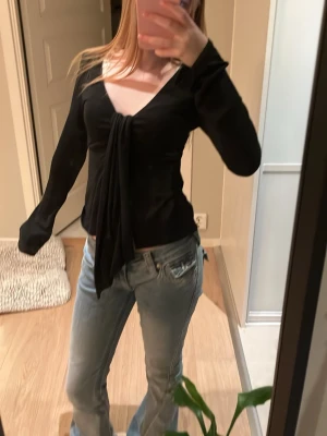 Svart tröja med knut - Trendig svart topp med knut, långa ärmar. Skönt material och bekvämt. Perfekt att matcha med jeans eller kjol för en uppdaterad outfit.