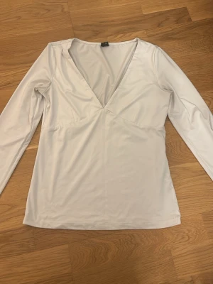 Vit långärmad v-ringad topp - Snygg vit långärmad topp med djup v-ringning och figurnära passform. Tillverkad i ett mjukt och stretchigt material som känns skönt mot huden. Perfekt att styla med jeans eller kjol för en clean look.