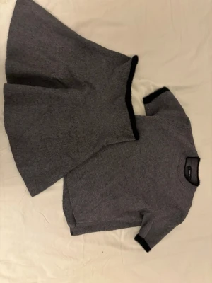 Grått set med kjol och topp - Säljer ett stilrent grått set från ZARA med en kortärmad topp och matchande kjol. Båda plaggen har svarta detaljer vid ärmslut, halsringning och midja. Materialet är mjukt och skönt. Perfekt för dig som gillar enkel men snygg design.