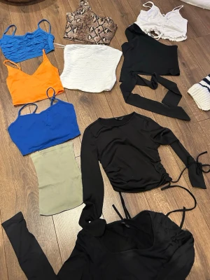 Mix av trendiga toppar i olika färger xs ca i strl  - Säljer ett paket med flera snygga toppar i olika färger och modeller. Inkluderar bland annat en ormskinnsmönstrad oneshoulder topp, croppade linnen i blått, orange och vitt, samt svarta långärmade toppar med snörning och omlottdetaljer. Perfekt för dig som vill uppdatera garderoben! Blandad strl xxs /  xs / s 