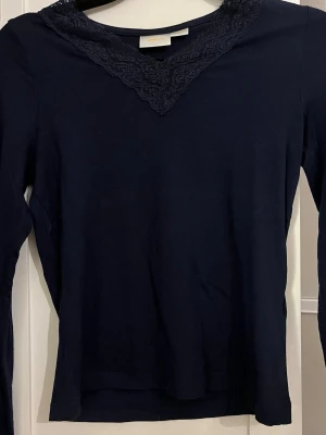 Mörkblå långärmad topp med spets - Mörkblå långärmad topp med v-ringning och snygg spetsdetalj runt halsen. Figurnära passform och mjukt material som känns skönt mot huden. Perfekt att styla med jeans eller kjol för en clean look.⭐️storleken på toppen är 146-152, skulle säga att det är som XXS-XS💕Toppen är i ett jättebra skick!