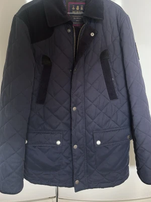 Quiltad jacka från Morris, marinblå - Snygg quiltad jacka från Morris i marinblått med detaljer i manchester på krage och axlar. Jackan har två stora fickor framtill, knappar och dragkedja. Perfekt för dig som vill ha en klassisk och stilren look. Tvättad på kemtvätt inför försäljning. Något stor i storleken och passar även för medium 