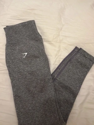 Grå leggings från Gymshark - Snygga grå leggings från Gymshark med hög midja och logga på låret. Tillverkade i ett stretchigt och mjukt material som passar perfekt till träning.